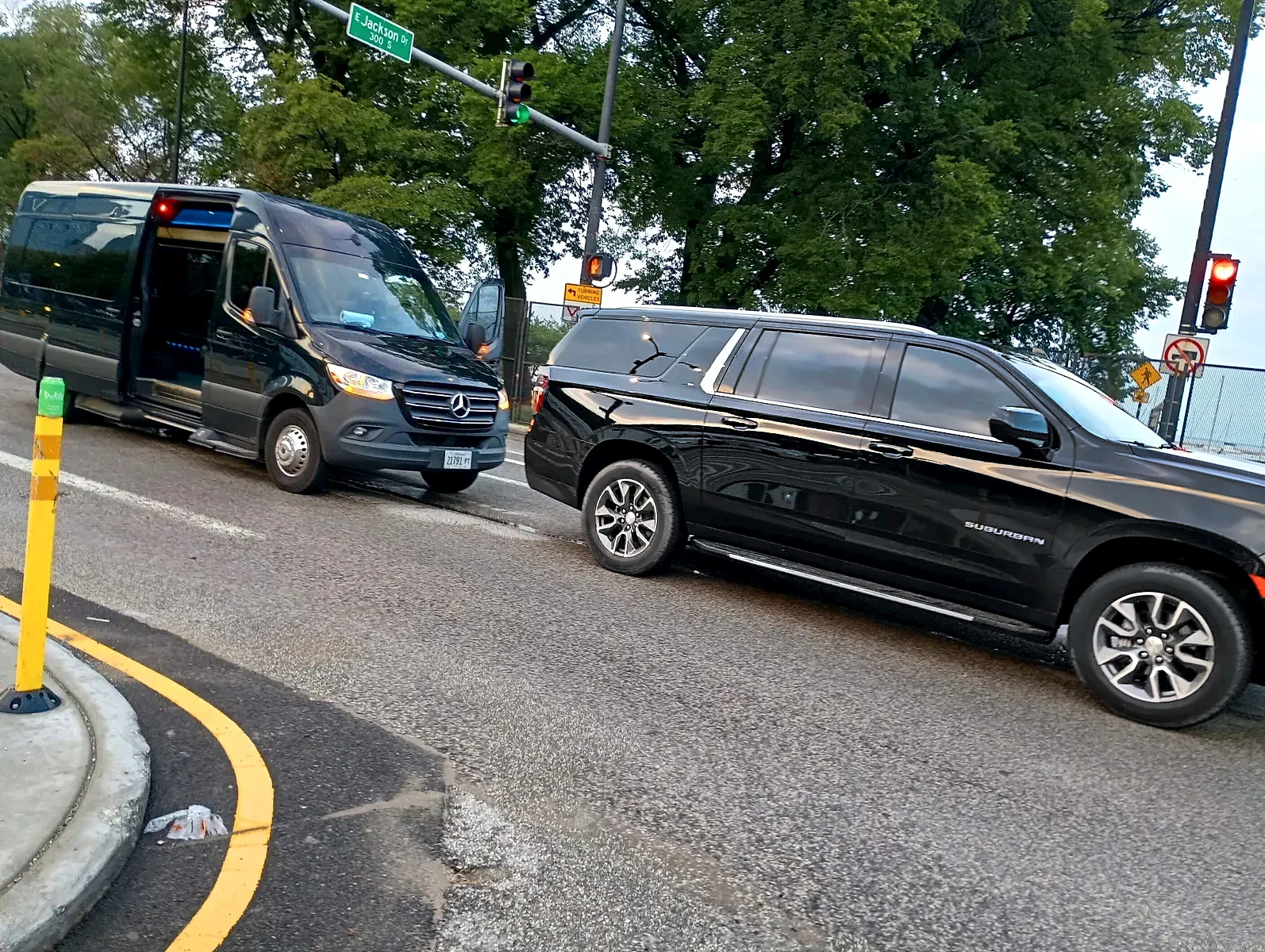 Black Mercedes Sprinter and black Chevrolet Suburban at the curb
